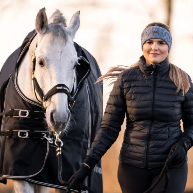 Blonde lady wearing light grey cable knit headband leading a grey horse in a werano halter